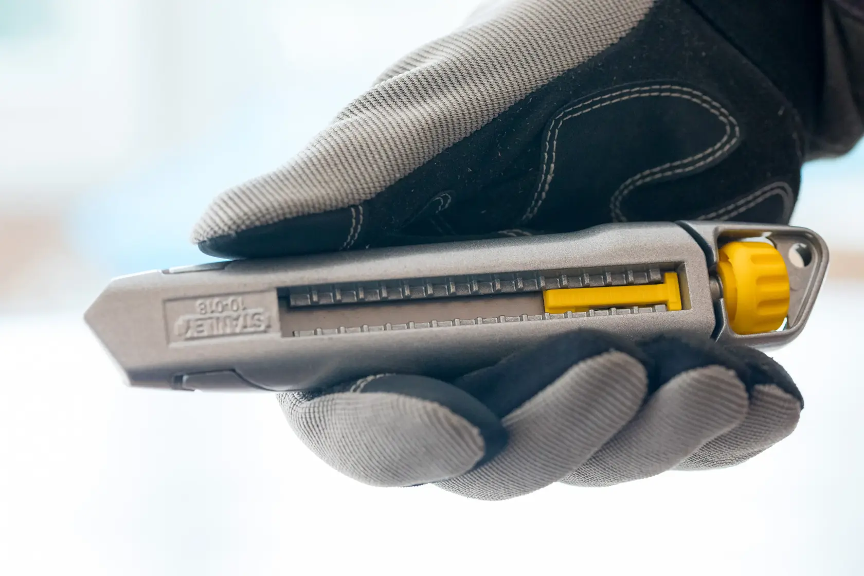 Foto des STANLEY 0-10-018 Cuttermessers in Grau und Gelb, mit Handschuh gehalten, Seitenansicht.