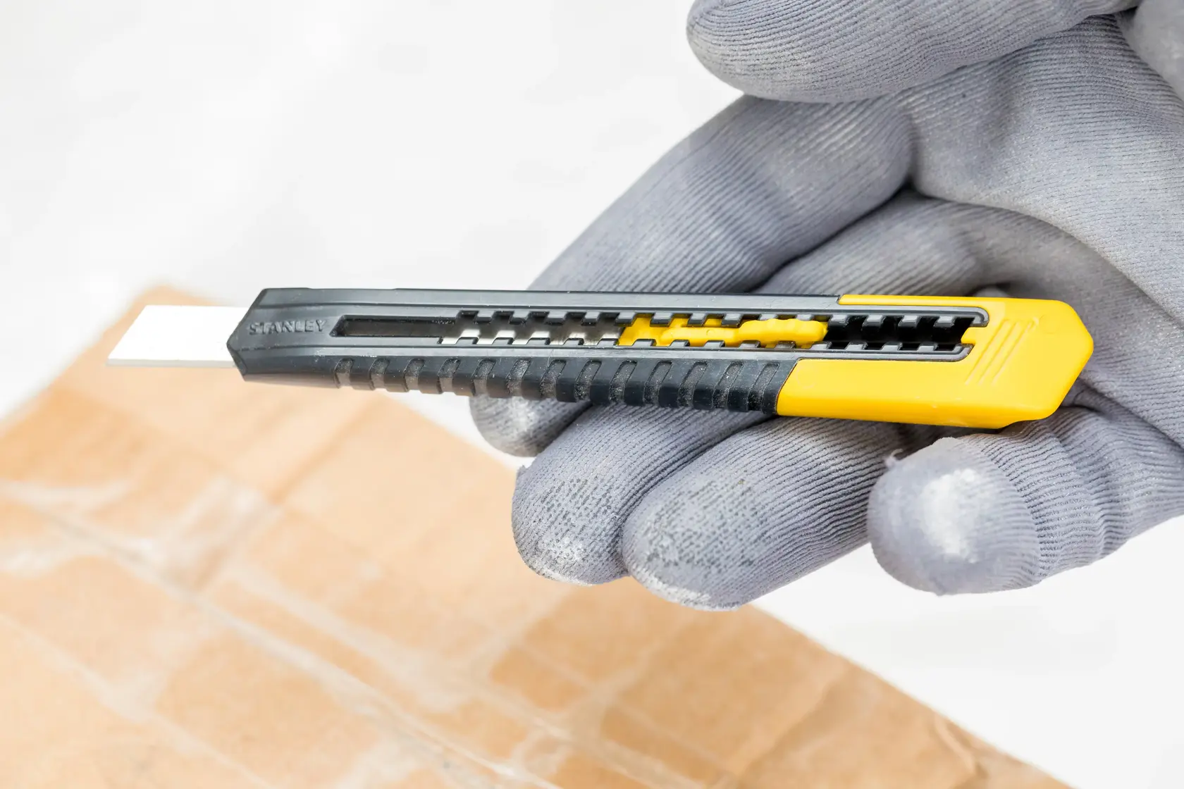 STANLEY 0-10-150 Universalmesser in Schwarz-Gelb, mit Handschuh über Karton gehalten.