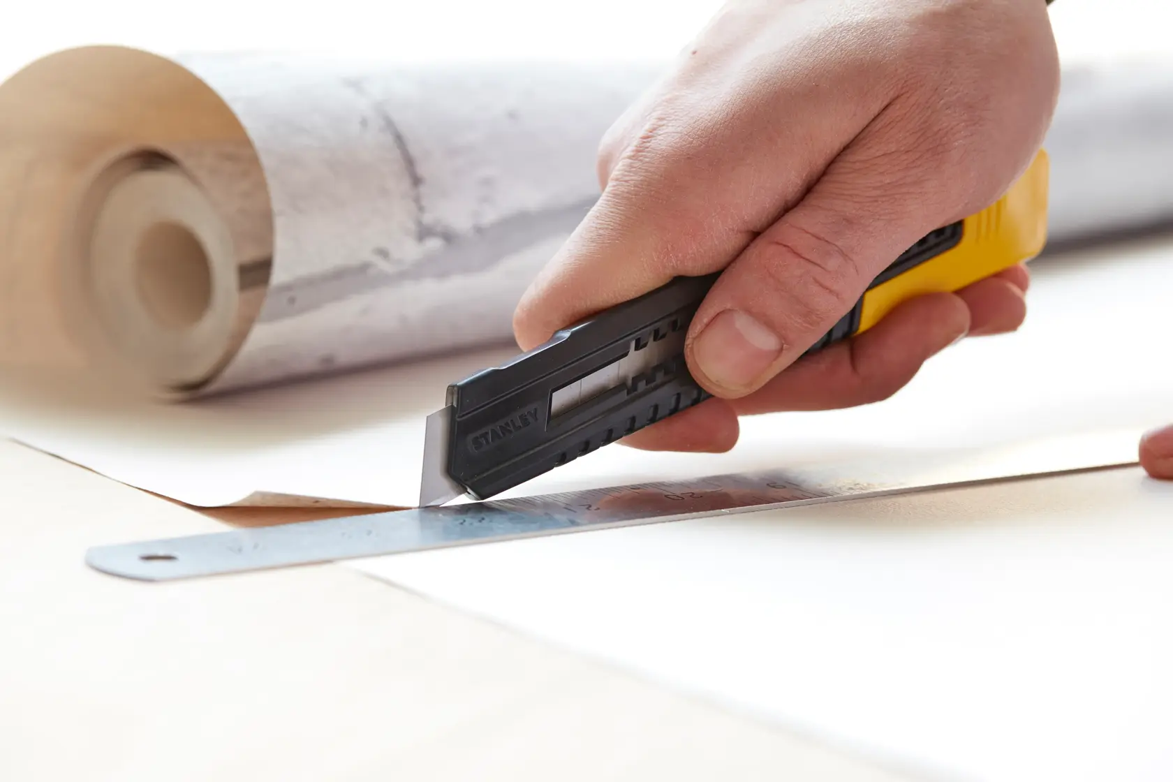 STANLEY 0-10-151 Universalmesser schneidet Tapete mit Lineal, Nahaufnahme, Hand hält Werkzeug.