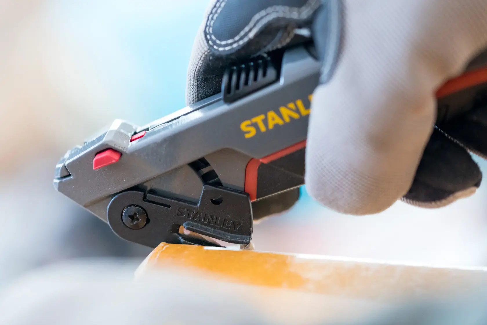 STANLEY 0-10-242 utility knife in use, close-up view, gloved hand holding tool, cutting material.