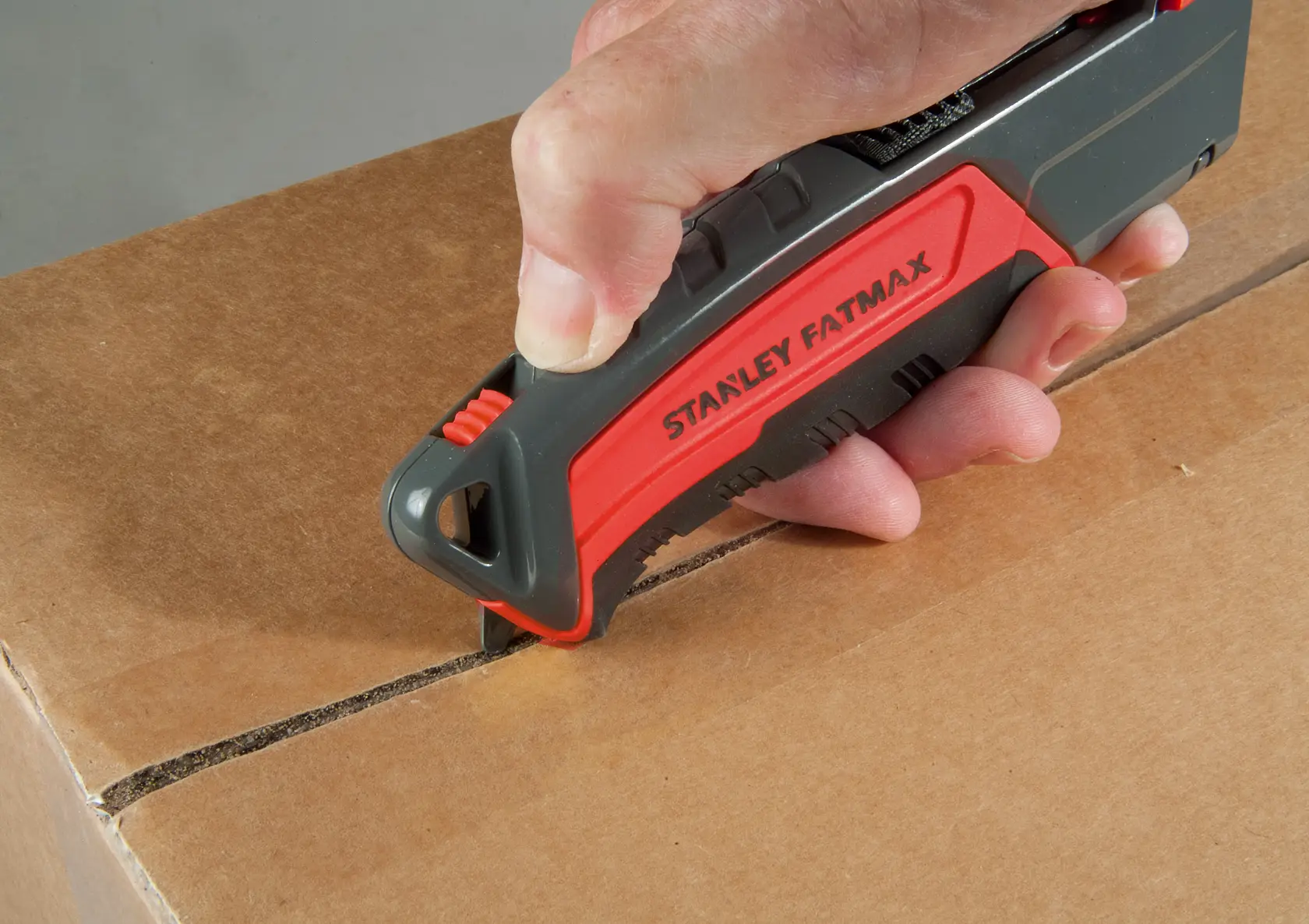 STANLEY 0-10-242 utility knife being used to cut a cardboard box, close-up of hand holding the red and black tool.