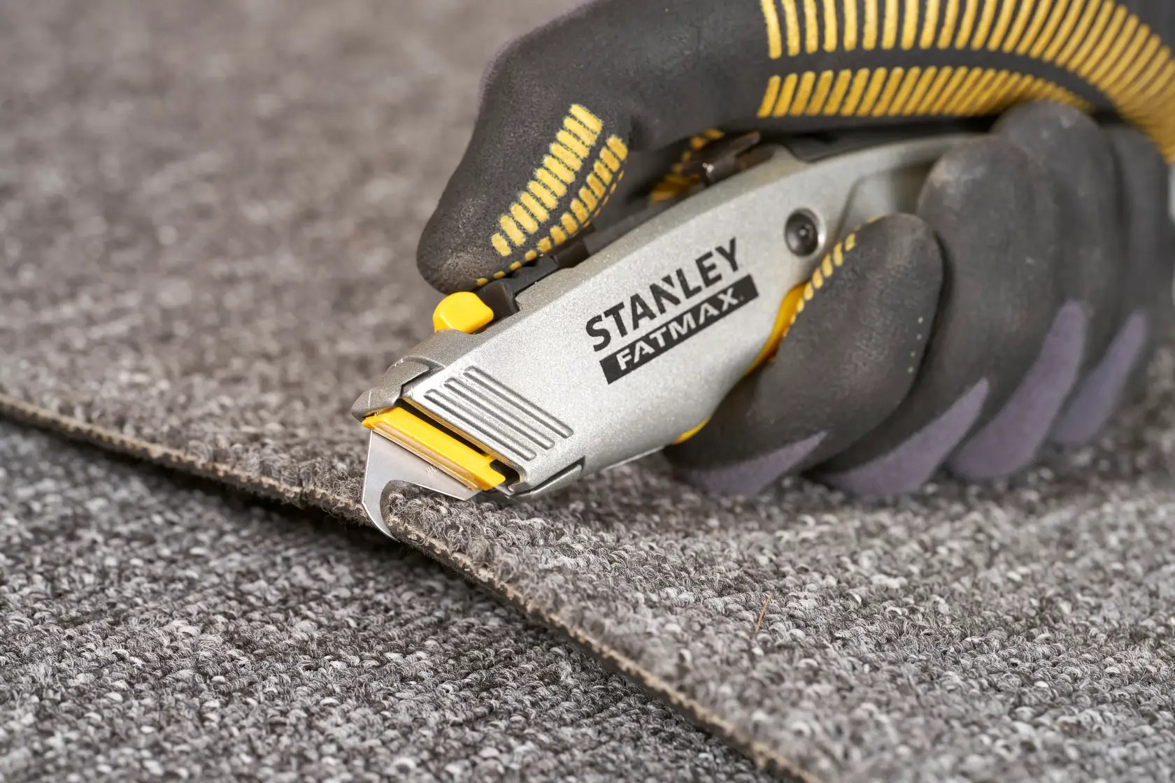 STANLEY 0-10-789 utility knife cutting carpet, close-up, grey and yellow handle.
