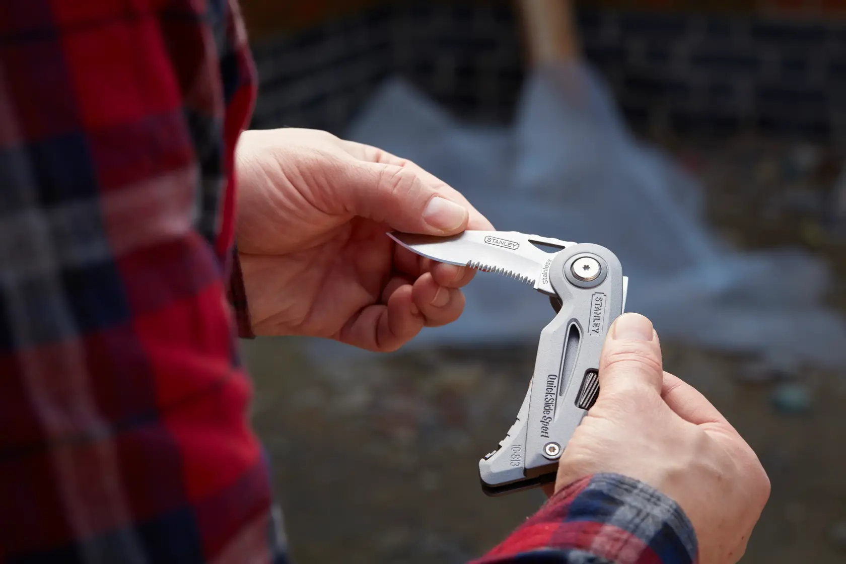 Foto vom STANLEY 0-10-813 Multitool-Messer, das im Freien gehalten und teilweise geöffnet mit Wellenschliff-Klinge gezeigt wird.