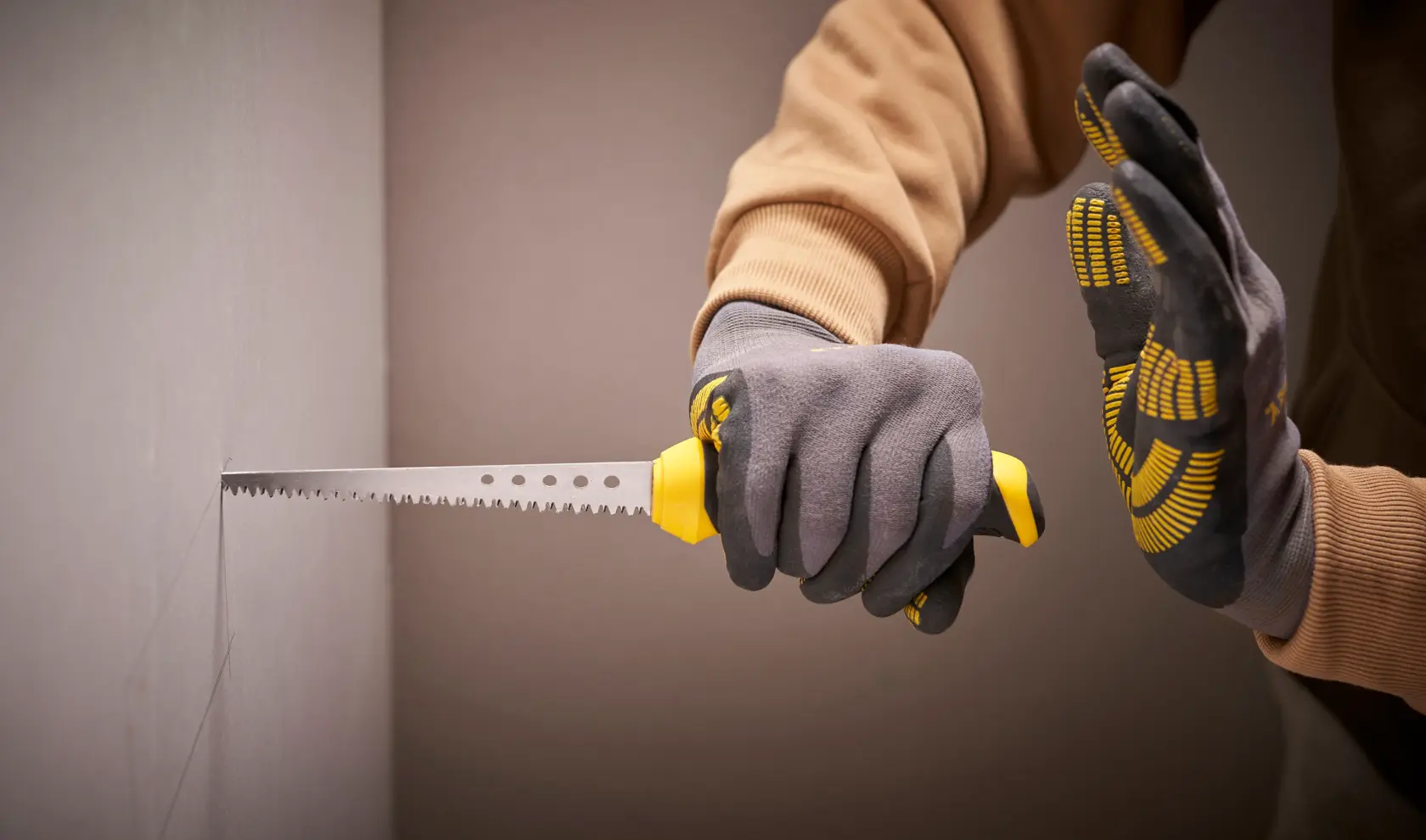 Photo of STANLEY 0-20-556 drywall saw used by gloved hands for cutting plasterboard, side angle.