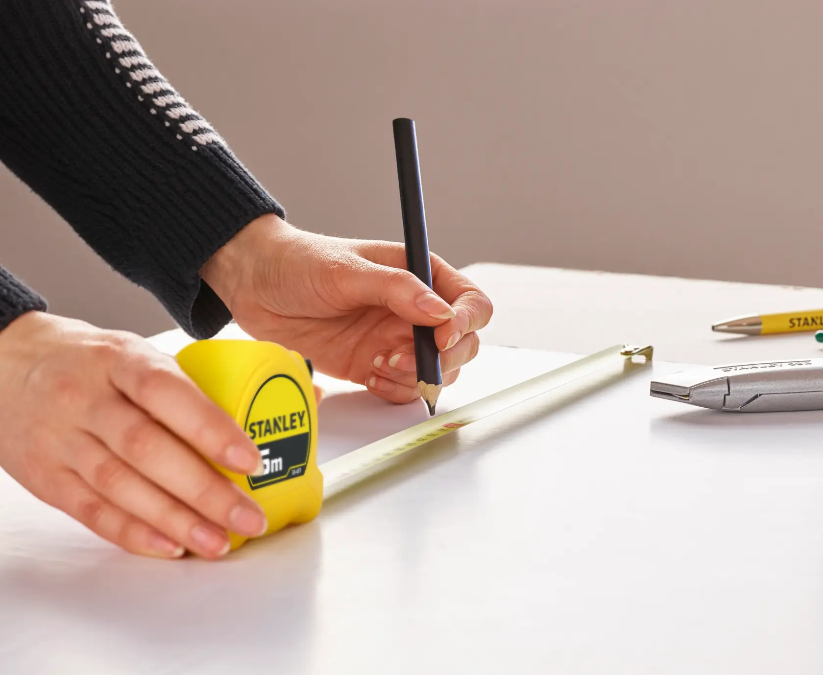 Photo of STANLEY 0-30-497 tape measure in use, close-up angled view, measuring and marking on white surface.