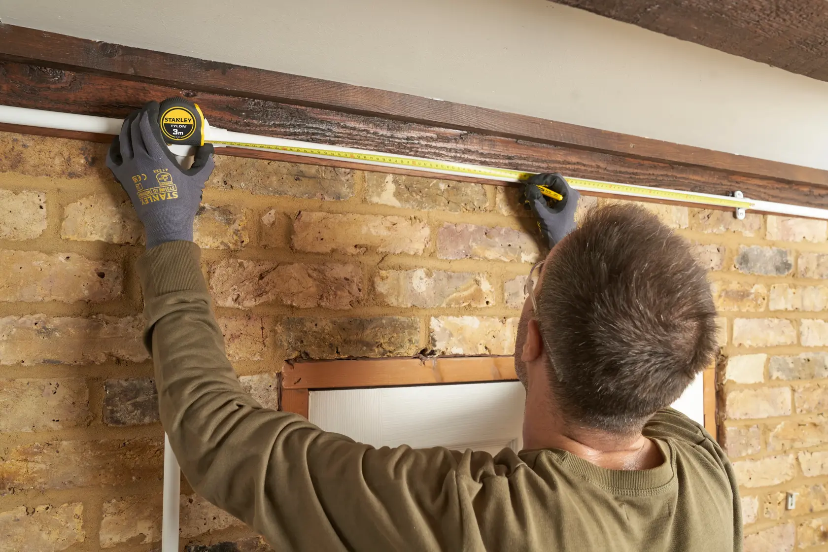 Photo of a person using a STANLEY 0-30-687 tape measure to measure a wall above a window indoors.