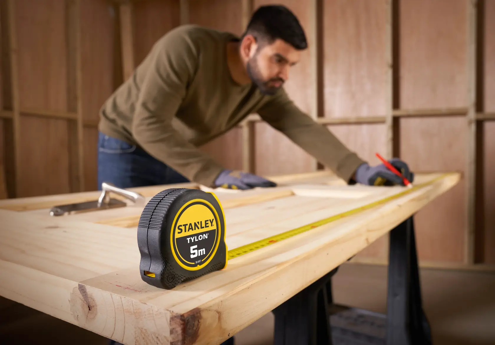 STANLEY 0-30-697 tape measure on wooden workbench with person marking wood, indoor workshop setting.
