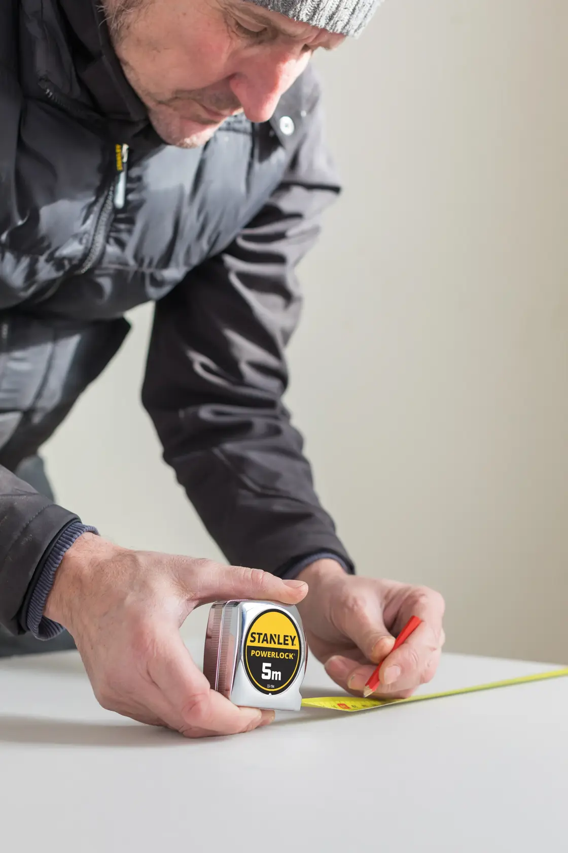 Photo of a person using a STANLEY 0-33-194 PowerLock 5m tape measure to mark a measurement on a white surface.