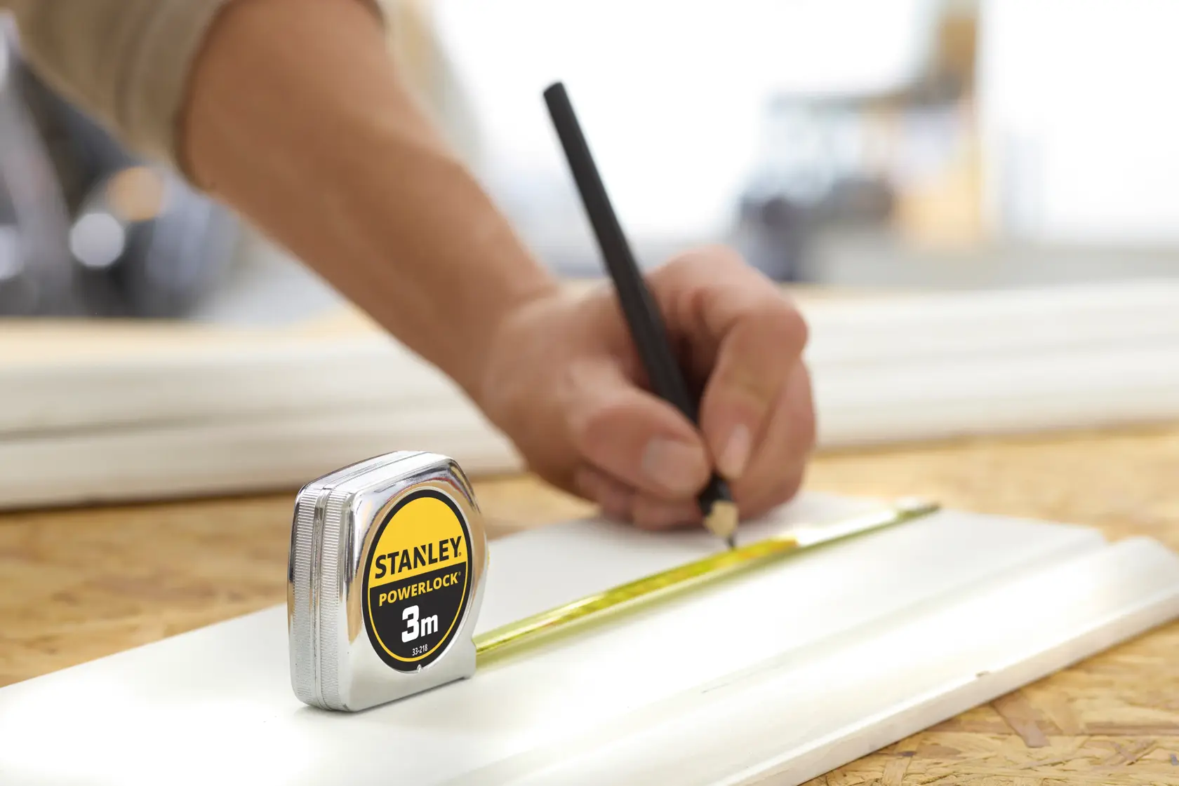 STANLEY 0-33-218 tape measure on wood surface, tape extended and person marking with pencil.