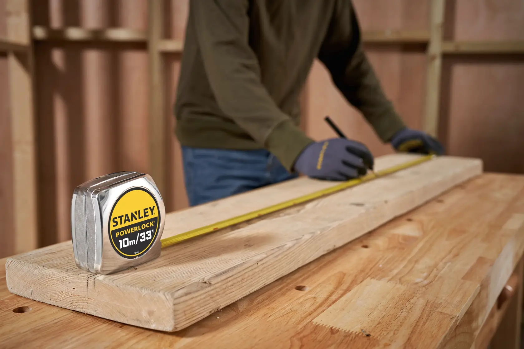STANLEY 0-33-443 tape measure on wooden board, person marking measurements in workshop.