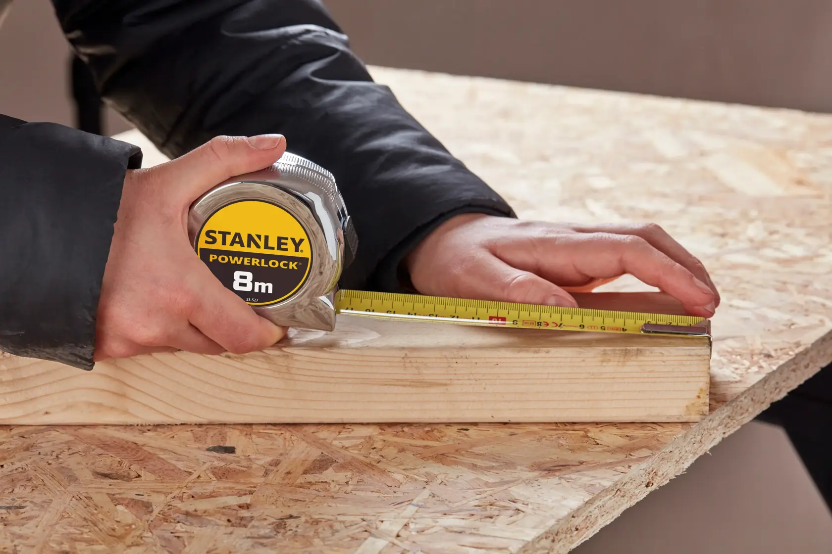 STANLEY 0-33-527 tape measure held measuring wood plank on work table, close-up photography.