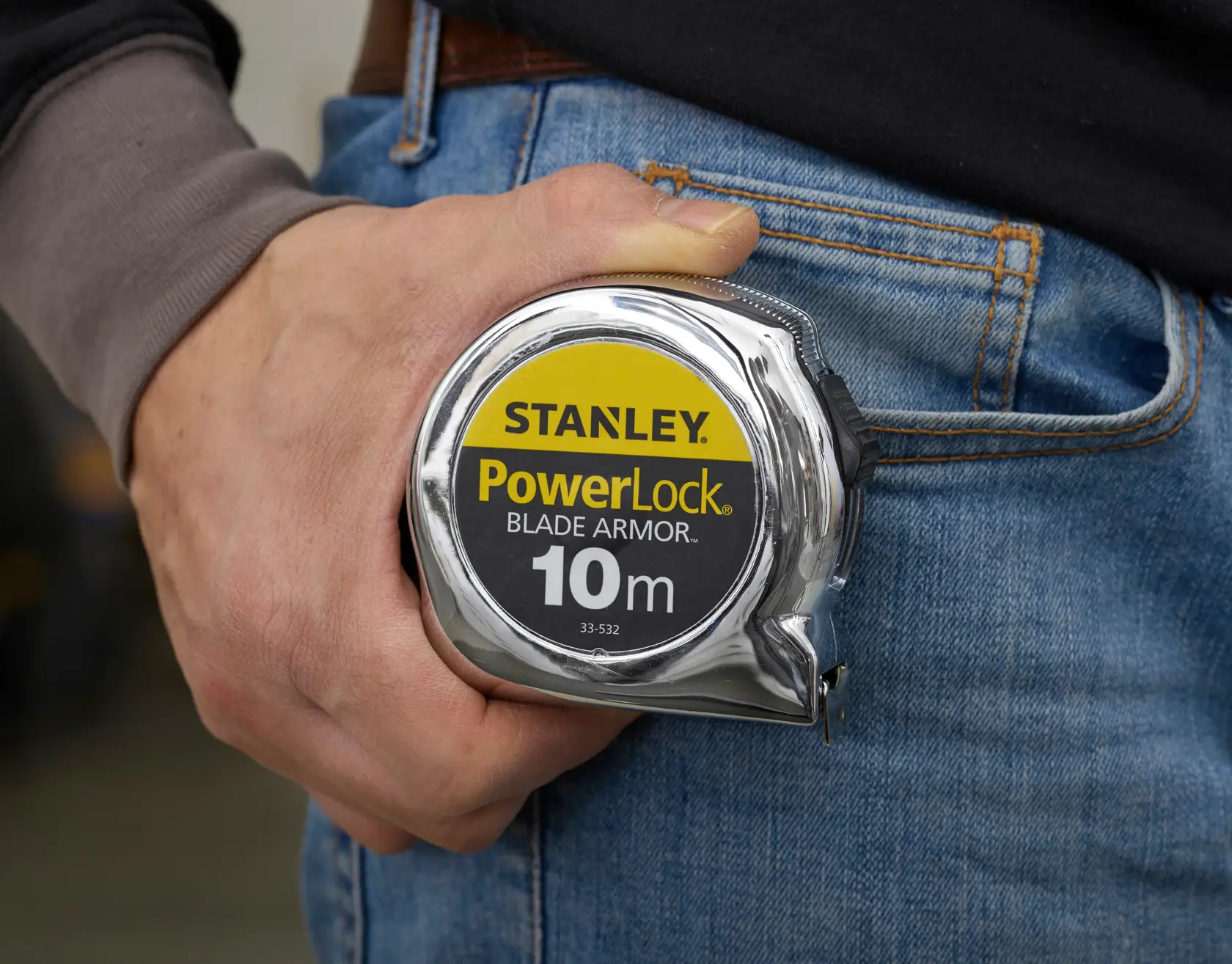 Photo of STANLEY PowerLock Blade Armor 10m tape measure SKU 0-33-532 held in a hand near blue jeans.