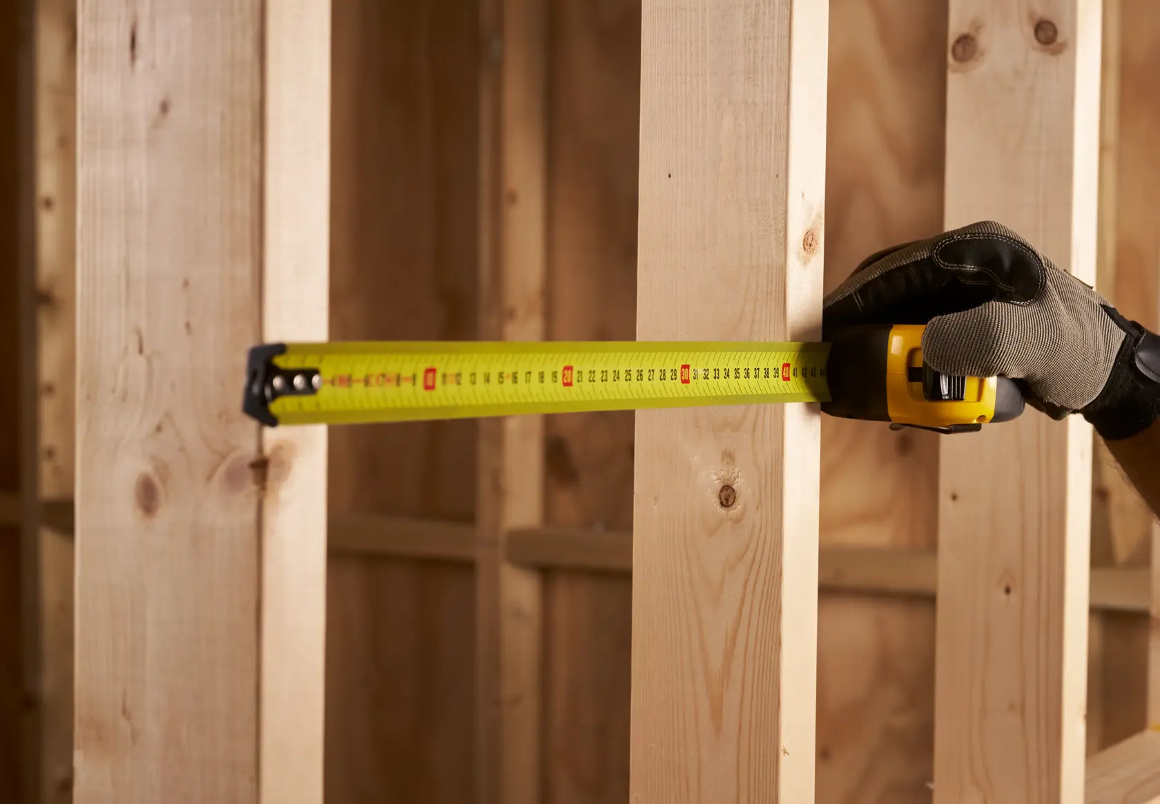 Photo of STANLEY 0-33-811 tape measure extended against wooden beams, held by gloved hand.