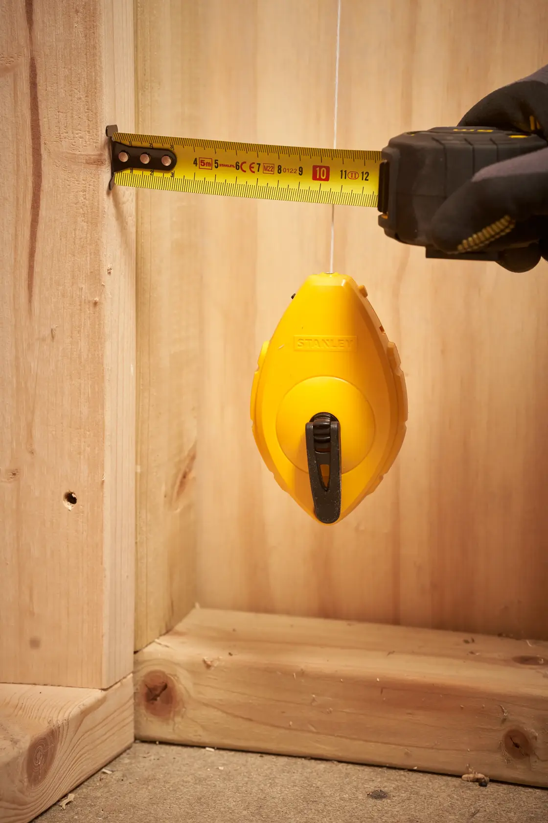STANLEY 0-47-440 Schlagschnurrolle im Einsatz mit Maßband an Holzrahmen, Nahaufnahme.