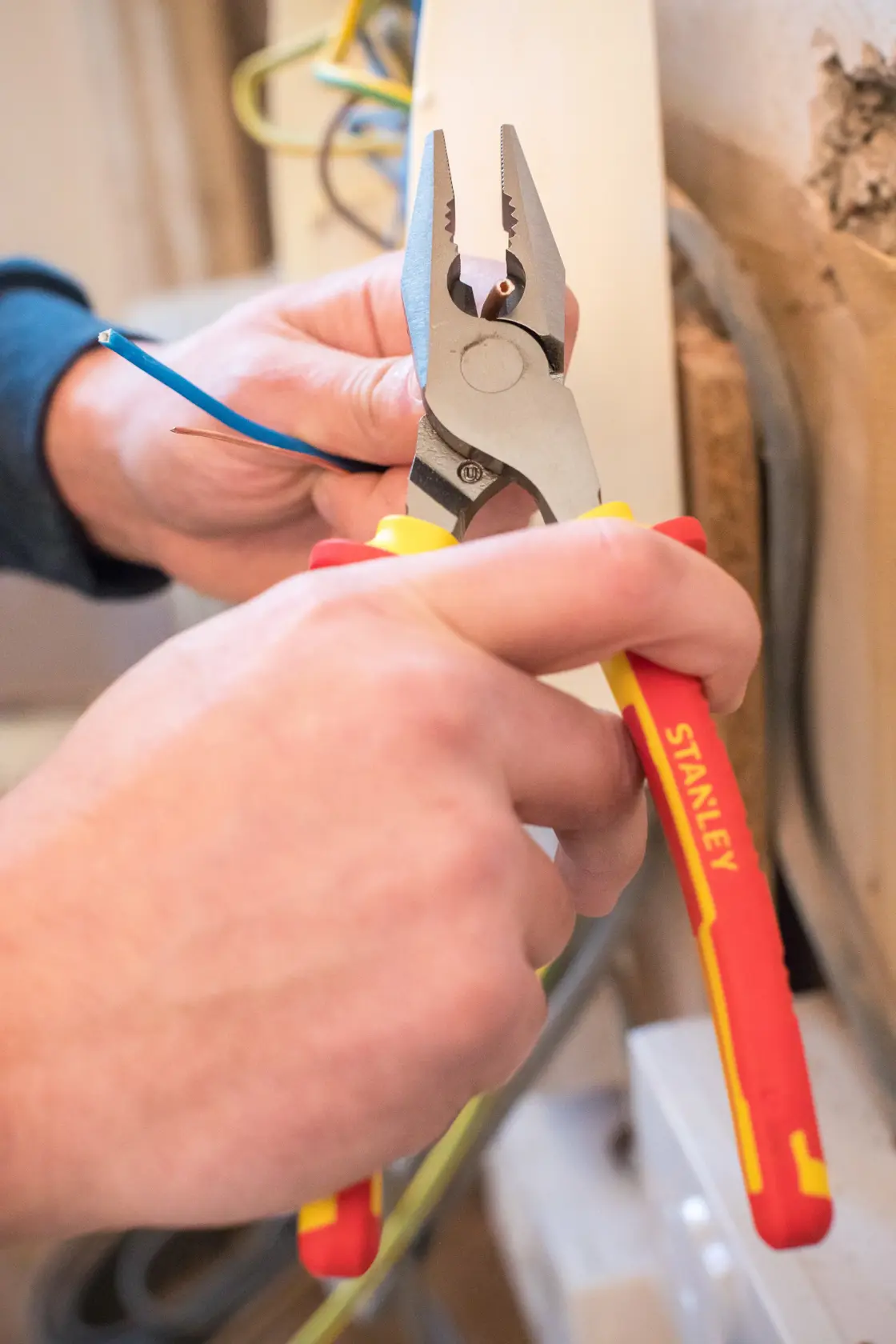 STANLEY 0-84-002 pliers with red and yellow handle cutting blue wire, close-up photo.