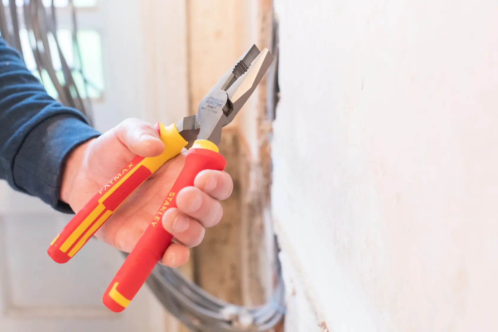 STANLEY 0-84-002 insulated pliers with red and yellow handles, used gripping wire near a wall.