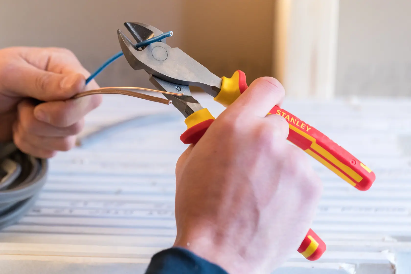 Photo of STANLEY 0-84-004 insulated wire cutters in use, cutting electrical cable, close-up view.