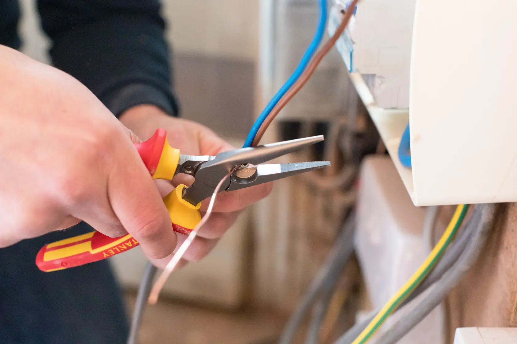 STANLEY 0-84-006 pliers with yellow-red handle used to strip wires by an electrician near a wall outlet.