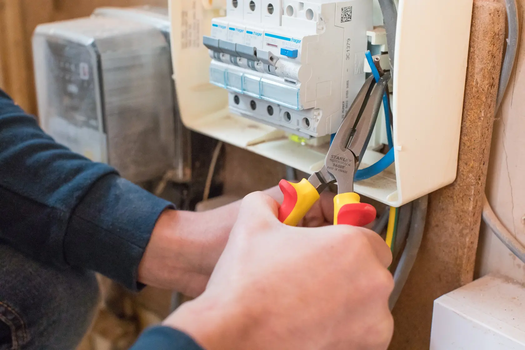 Photo of STANLEY 0-84-008 insulated pliers in use, gripping wire near electrical panel.