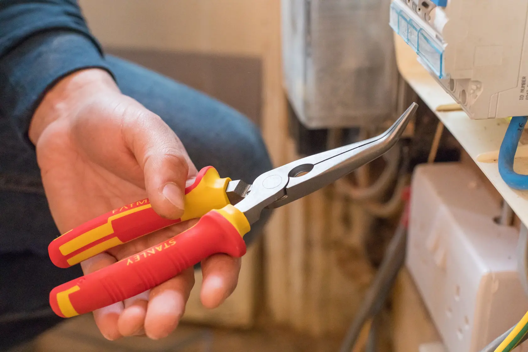 Photo of STANLEY 0-84-008 insulated bent long nose pliers with red and yellow handles in a hand.