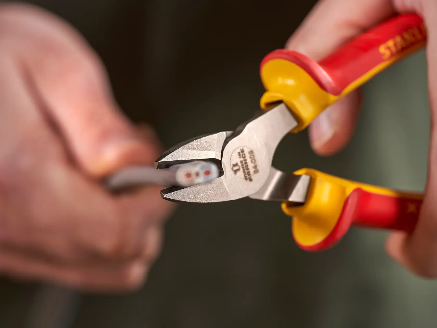 STANLEY 0-84-009 insulated diagonal cutting pliers with red and yellow handles cutting a wire, close-up.