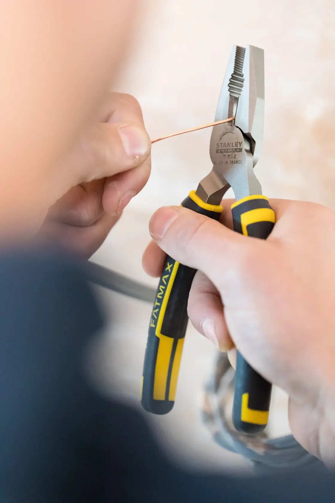 STANLEY 0-89-866 pliers with black and yellow handles gripping copper wire, close-up in hand.