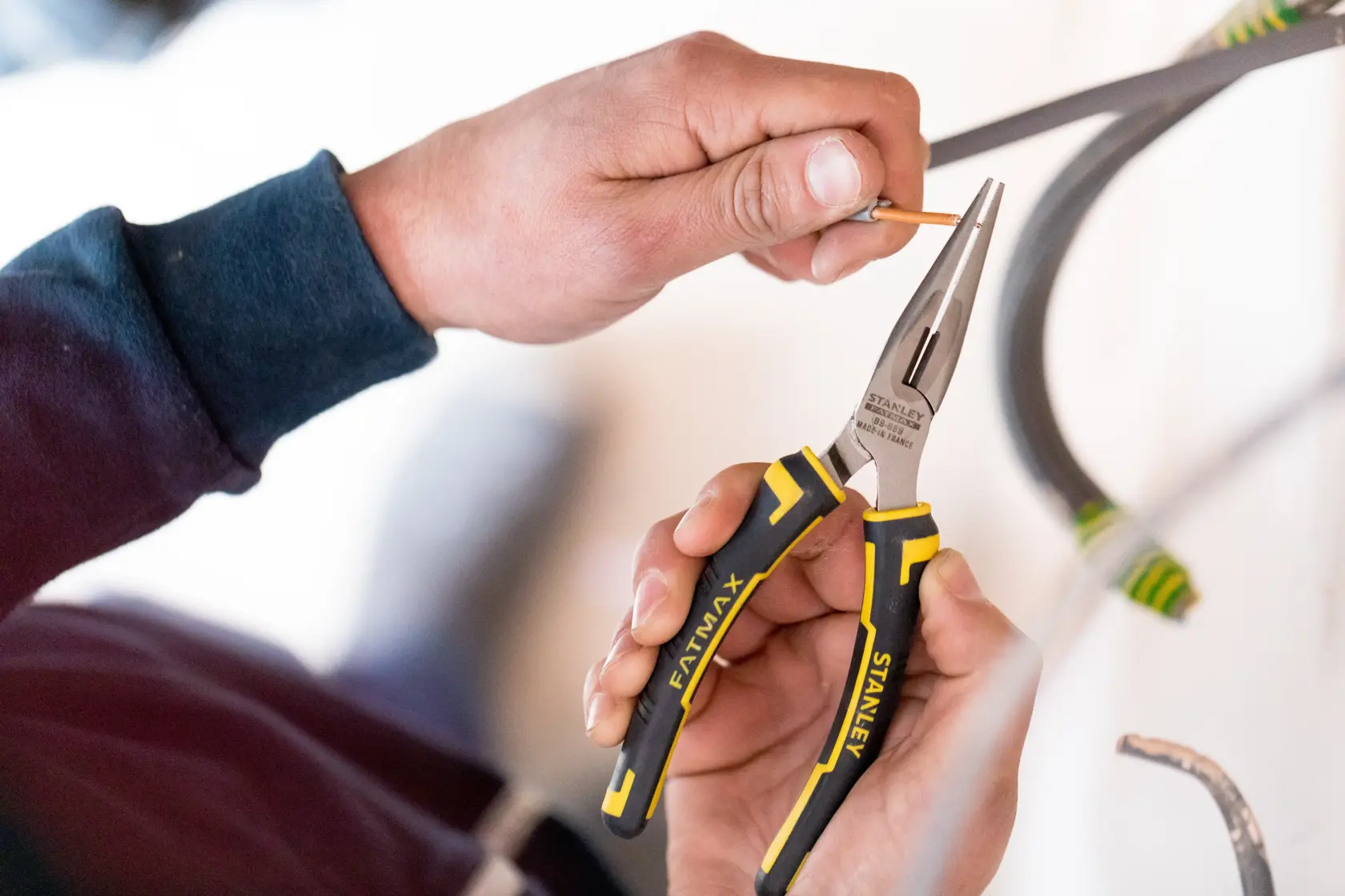 Photo of STANLEY 0-89-869 long nose pliers with black and yellow handle, held while gripping a wire, product in use.
