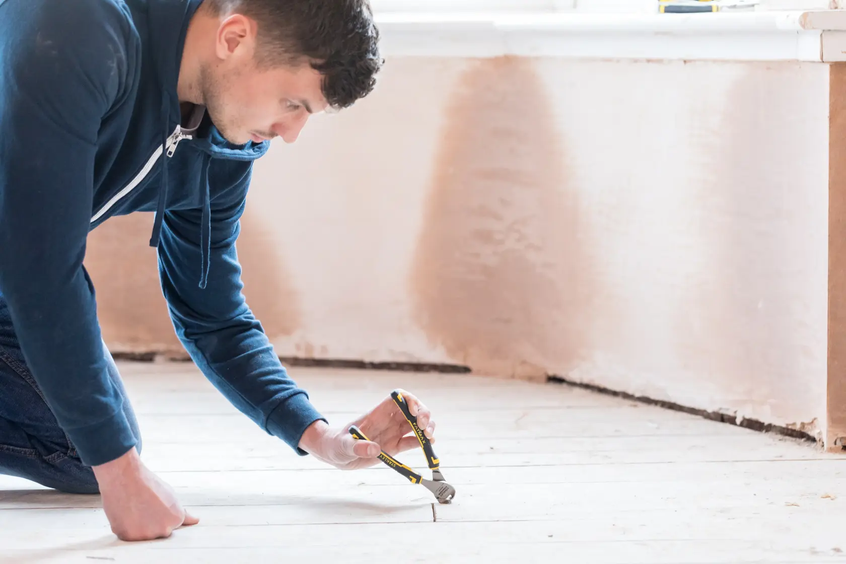 STANLEY 0-89-875 pliers in use pulling a nail from a wooden floor in a home renovation setting.
