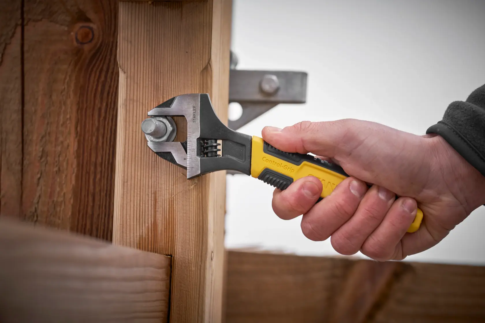STANLEY 0-90-947 adjustable wrench with yellow handle tightening a bolt on wooden beams, side angle.