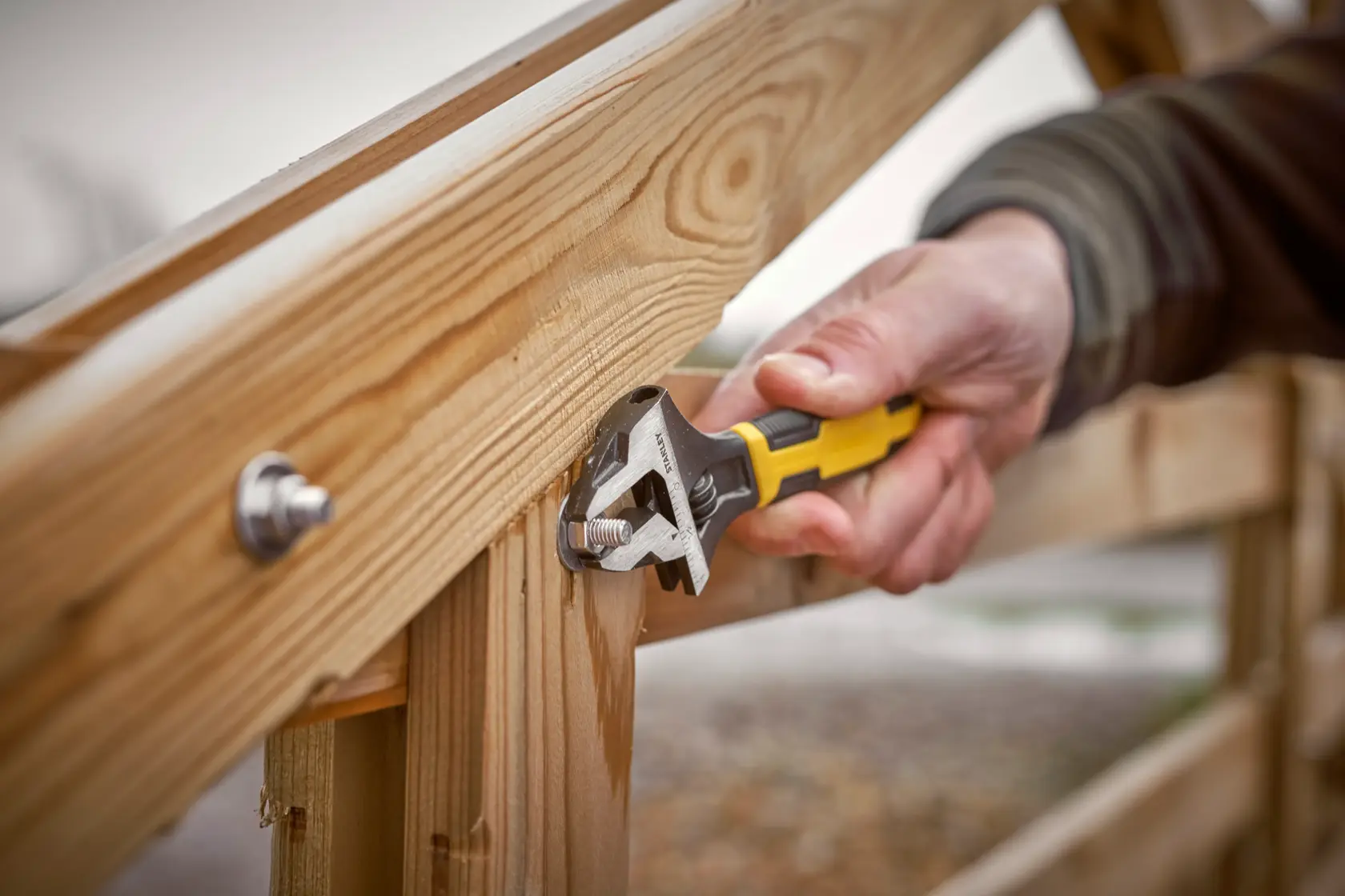 STANLEY 0-90-950 adjustable wrench with yellow handle, tightening bolt on wooden structure, close-up.