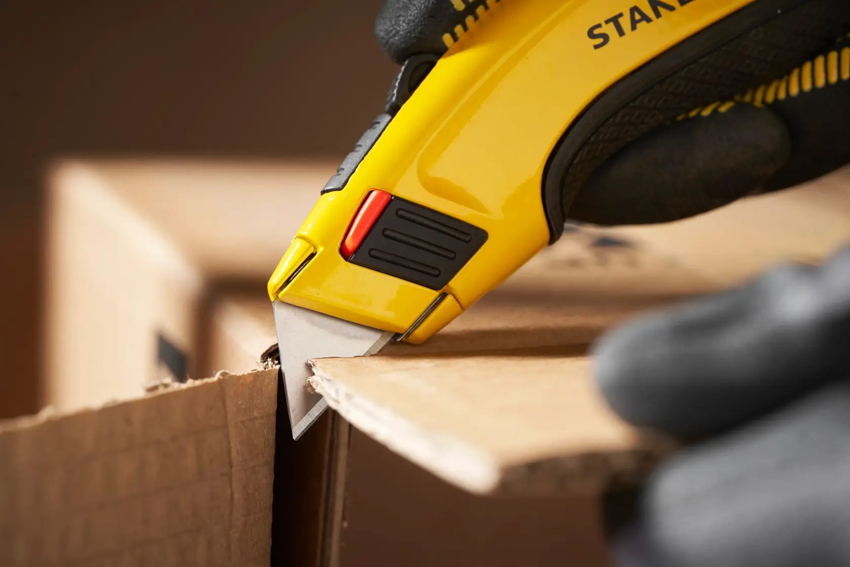 Stanley 1-11-700 utility knife cutting cardboard, close-up photography with glove holding tool.