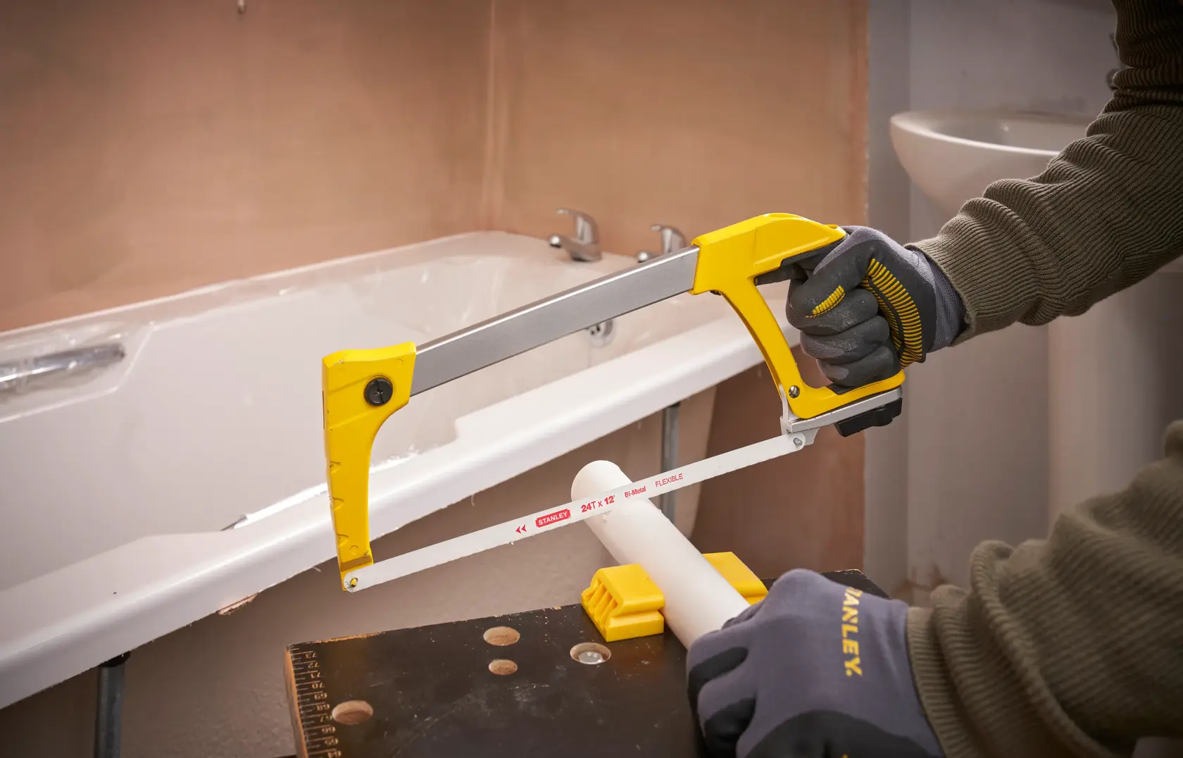 Photo of STANLEY 1-20-110 hacksaw used to cut white PVC pipe, close-up view in a bathroom setting.