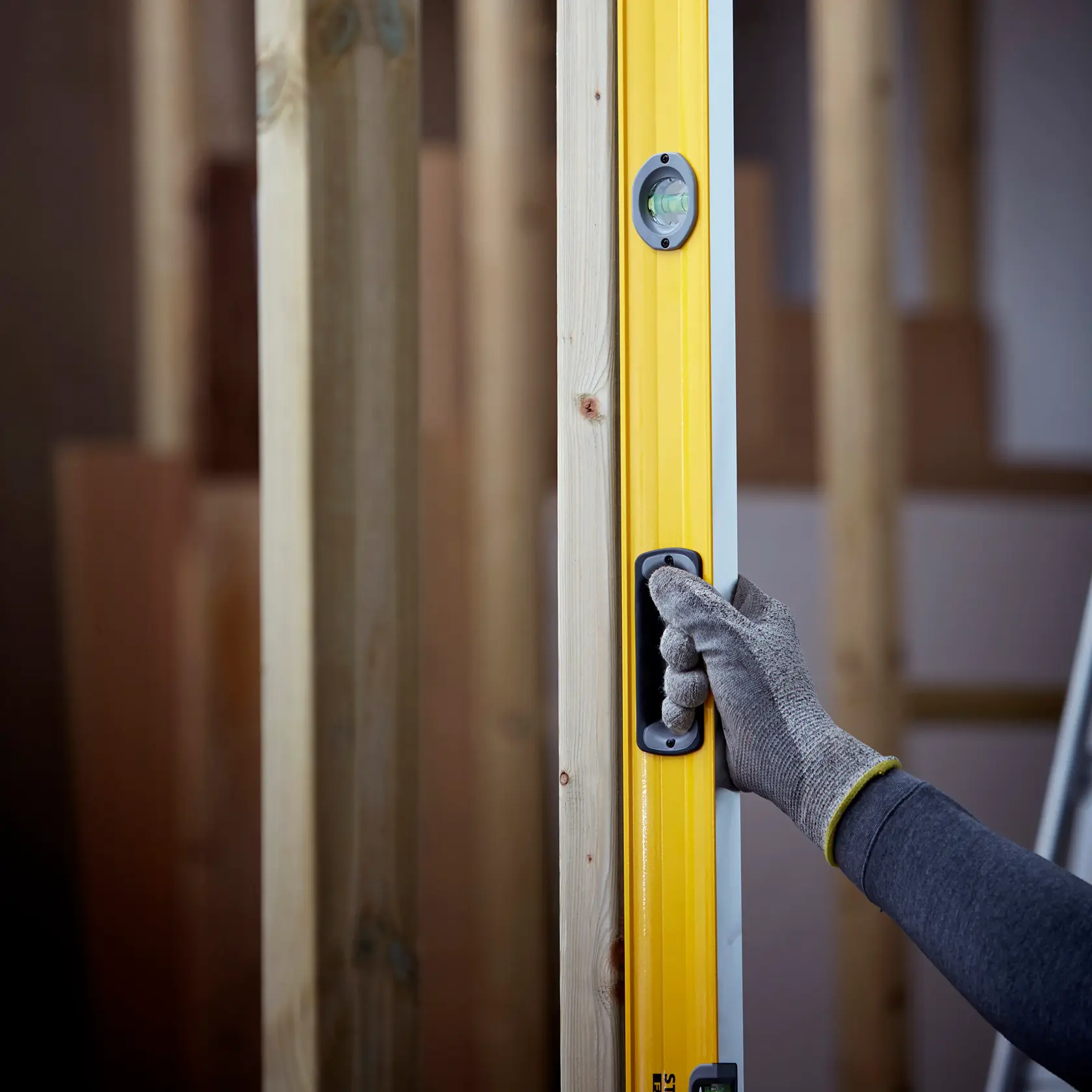 STANLEY 1-43-572 spirit level in use, yellow body with hand in work glove holding handle, construction background.
