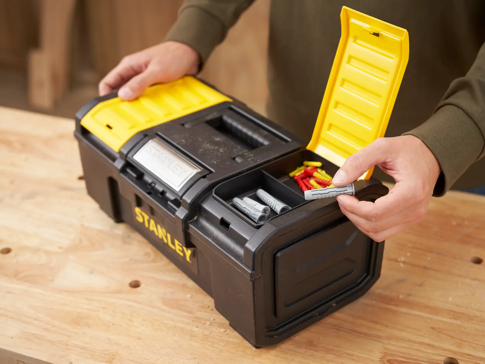 STANLEY 1-79-216 black and yellow toolbox with open compartment holding wall plugs, shown on a workbench.