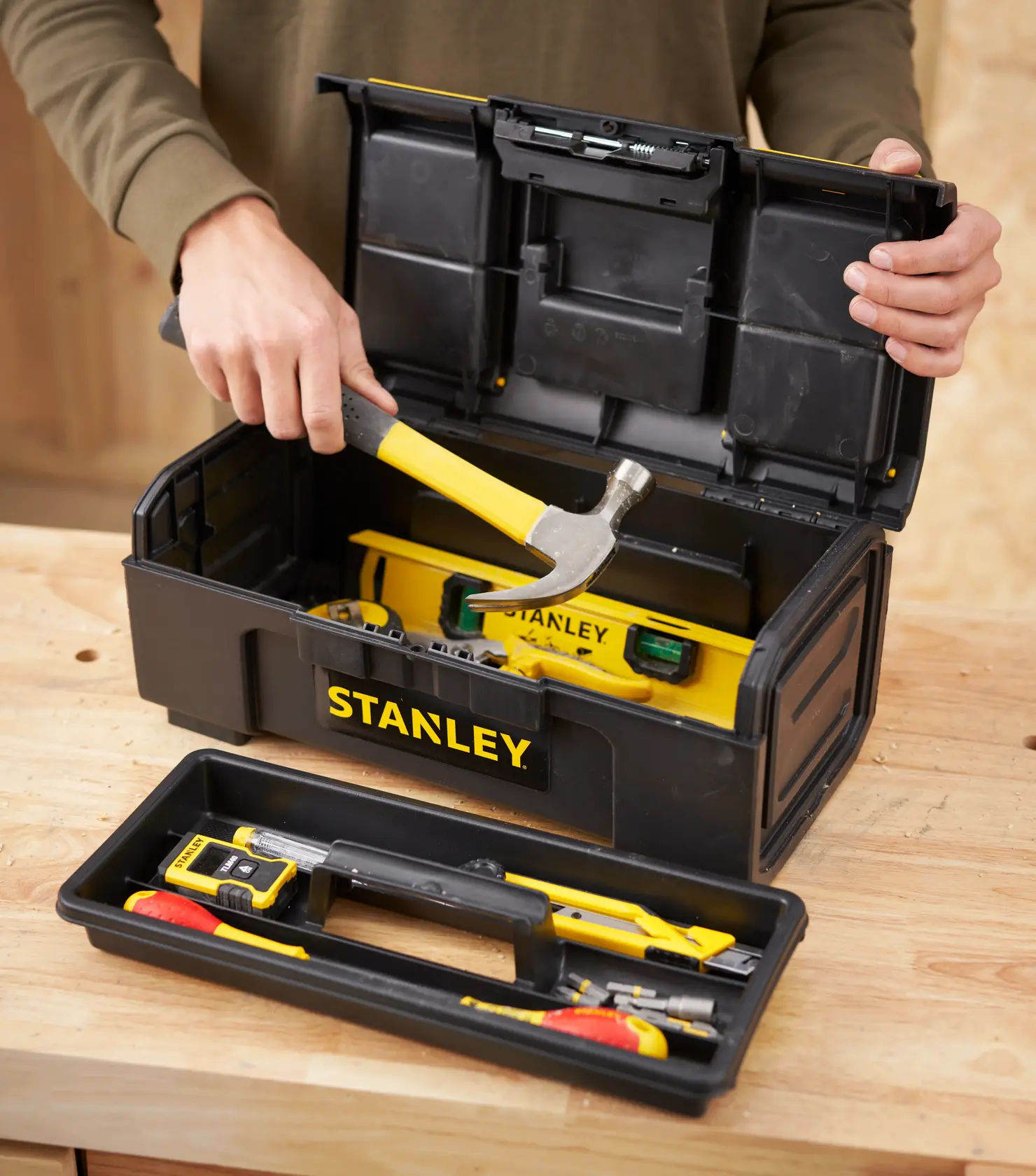 STANLEY 1-79-216 tool box with yellow tools including hammer and level, open on a workbench, front angle.