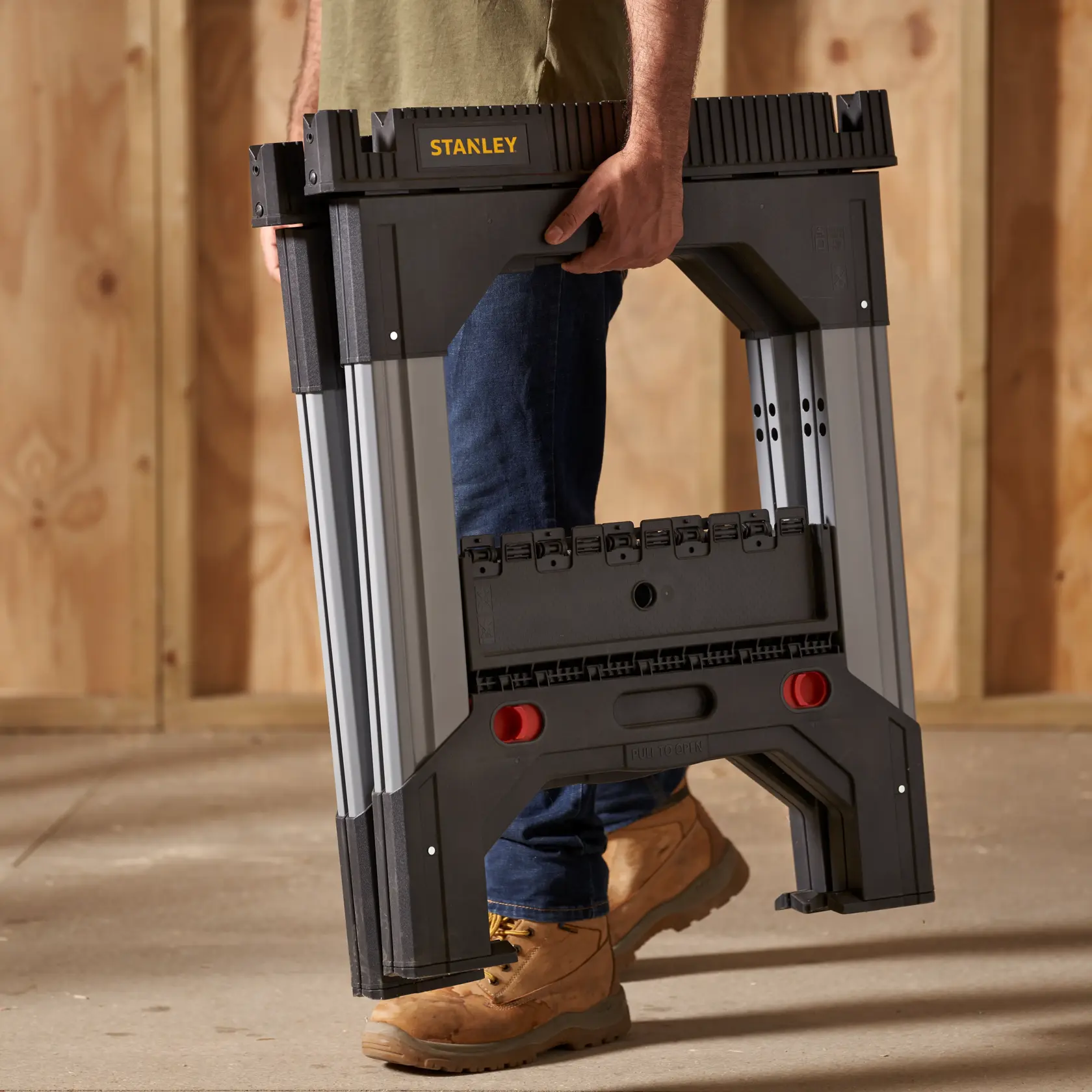 STANLEY 1-92-980 folding saw horse, black and silver, shown carried by a person, workshop setting.