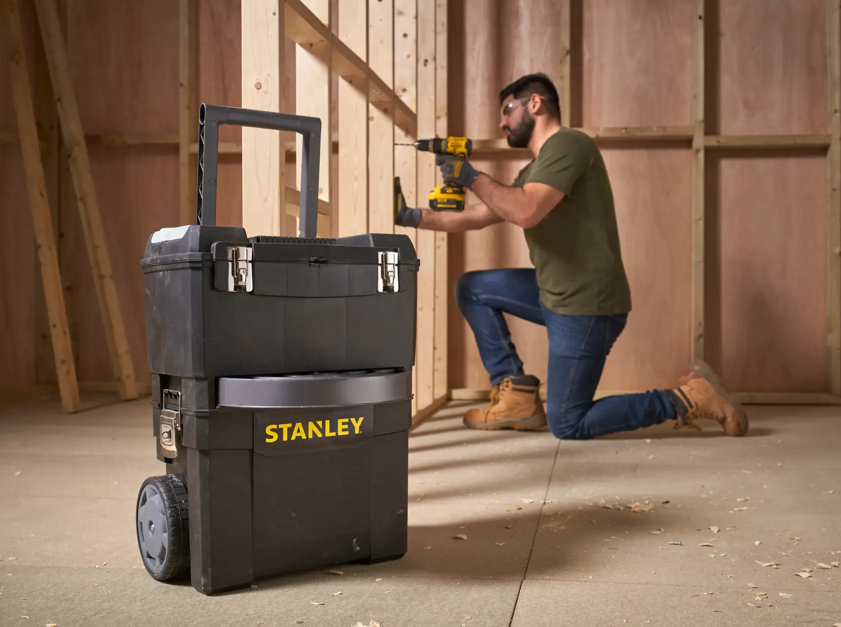 STANLEY 1-93-968 mobile tool chest with wheels in workshop, worker using power tool in background.
