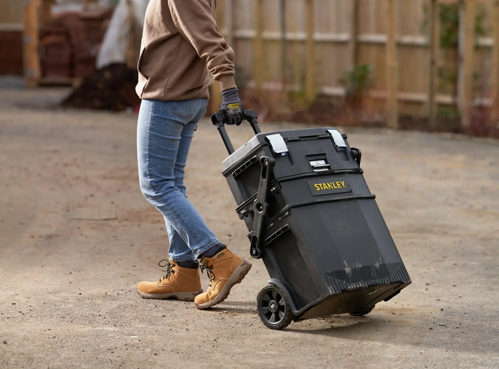 STANLEY 1-94-210 rolling toolbox being pulled outdoors by a person wearing jeans and work boots.