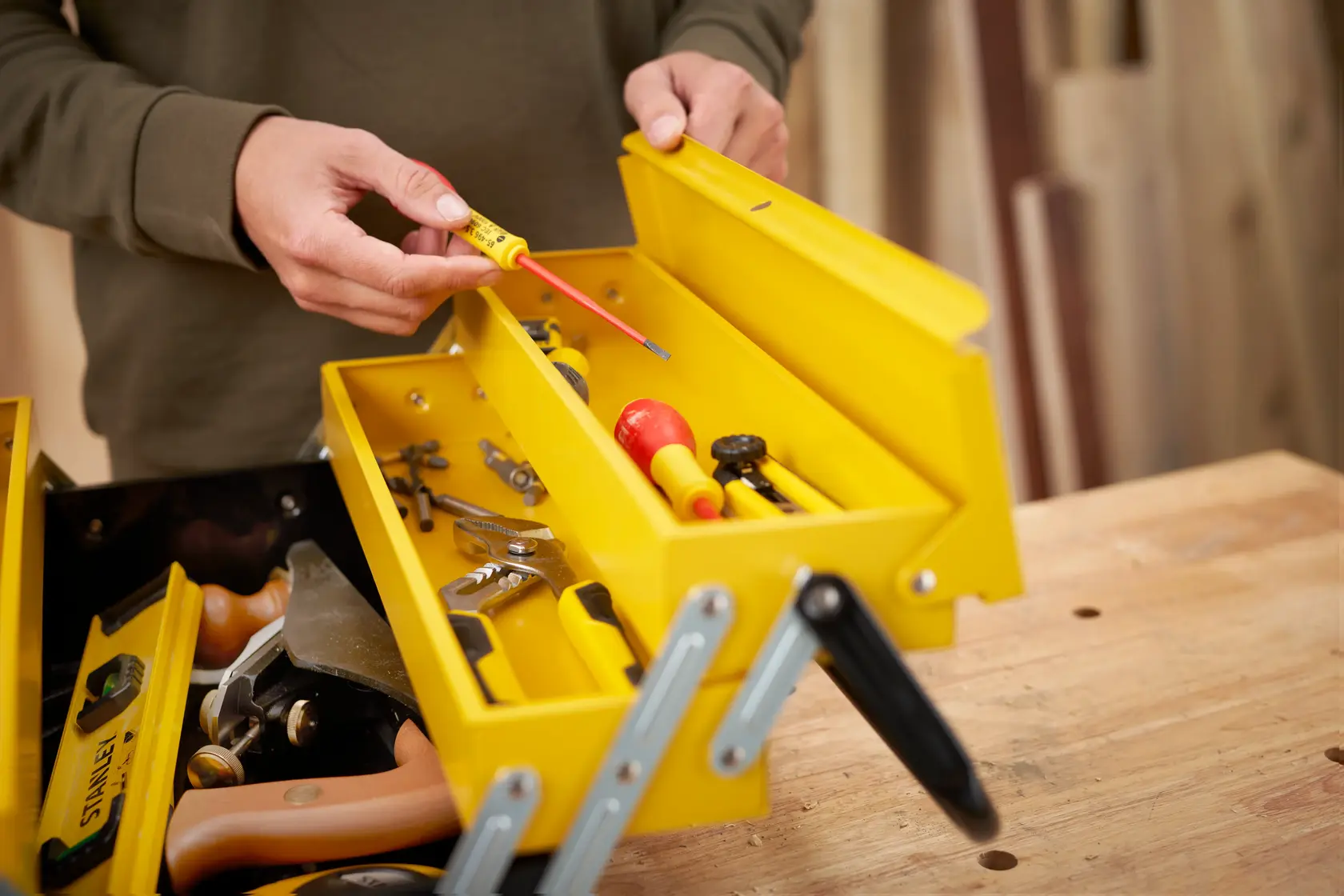 STANLEY 1-94-738 yellow metal toolbox with assorted hand tools, open on a wood table, angled view.