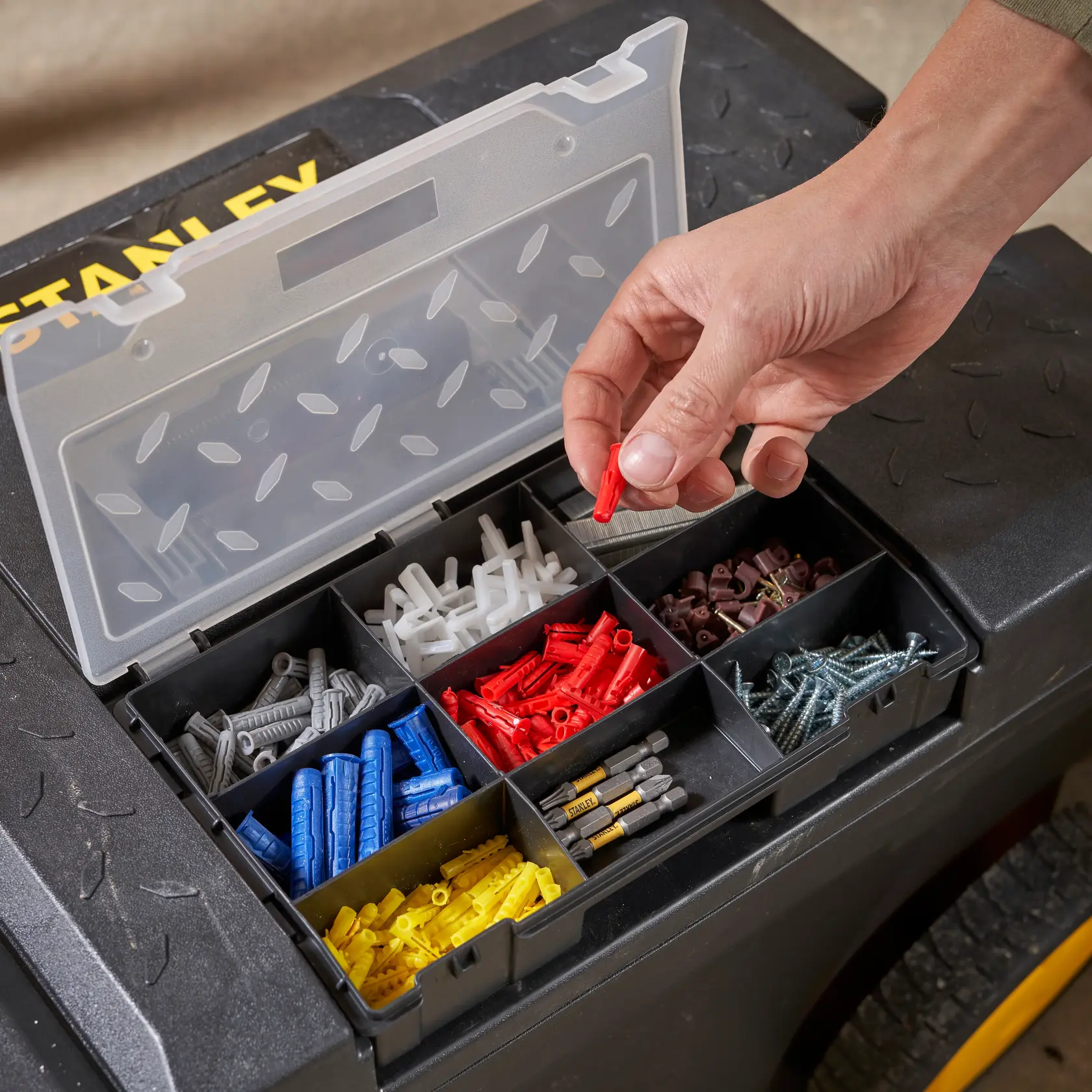 STANLEY 1-97-503 organizer top view with hand picking red wall plug, assorted screws and anchors in compartments.