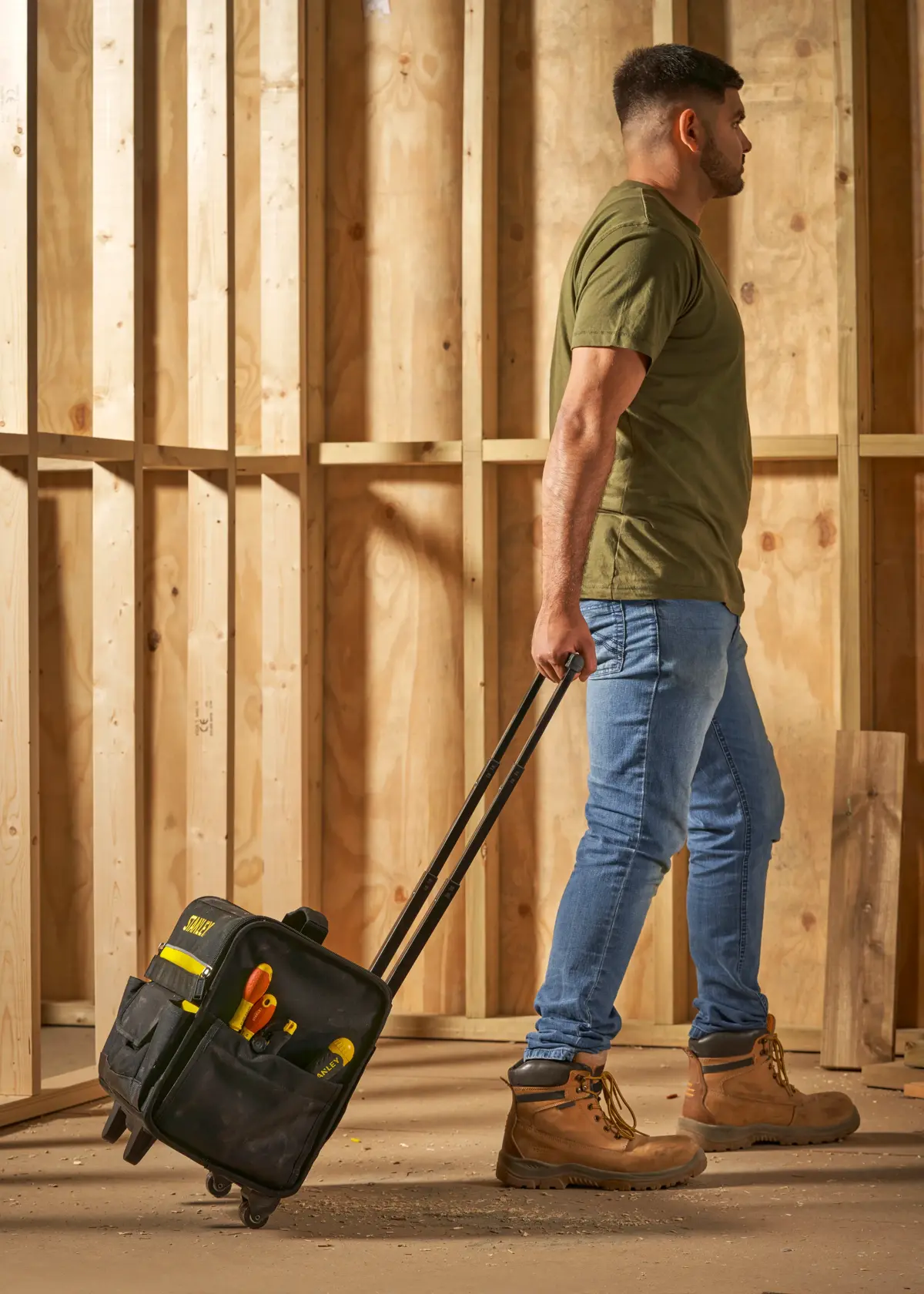 STANLEY 1-97-515 Rollwerkzeugtasche mit Werkzeugen, getragen von Person mit Arbeitsstiefeln auf Baustelle.