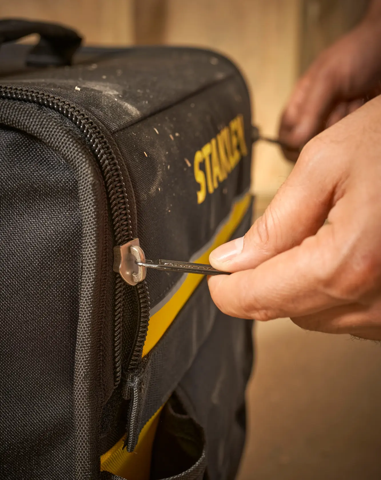 STANLEY 1-97-515 Werkzeugtasche Fotografie, Nahaufnahme von Hand am Reißverschluss auf schwarzer und gelber Tasche.