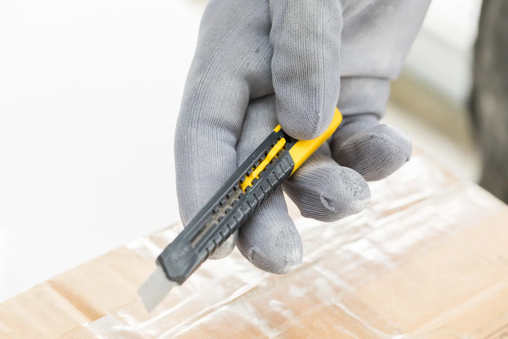 Photo of STANLEY 2-10-150 utility knife cutting tape on a cardboard box, held by a gloved hand.