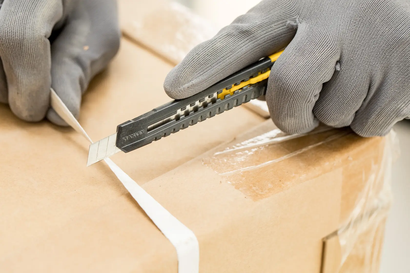 STANLEY 2-10-150 utility knife cutting box strap, close-up photo with gloved hands, product photography.
