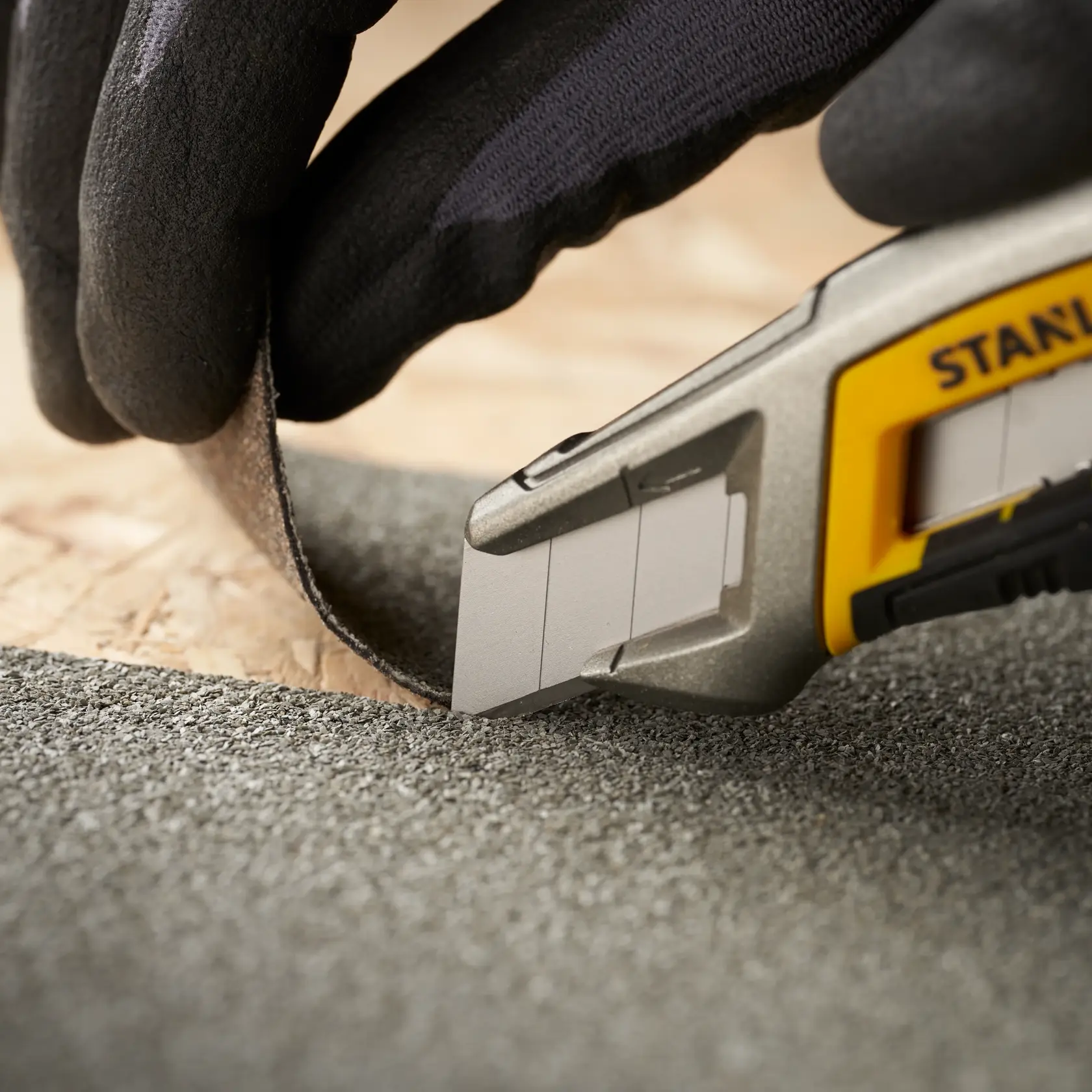 STANLEY 2-11-301 utility knife cutting rough material, close-up photo, gloved hand holding material.
