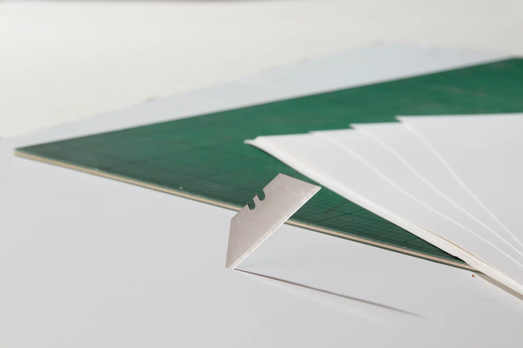STANLEY 2-11-700 utility blade close-up, beside green cutting mat and white paper sheets.