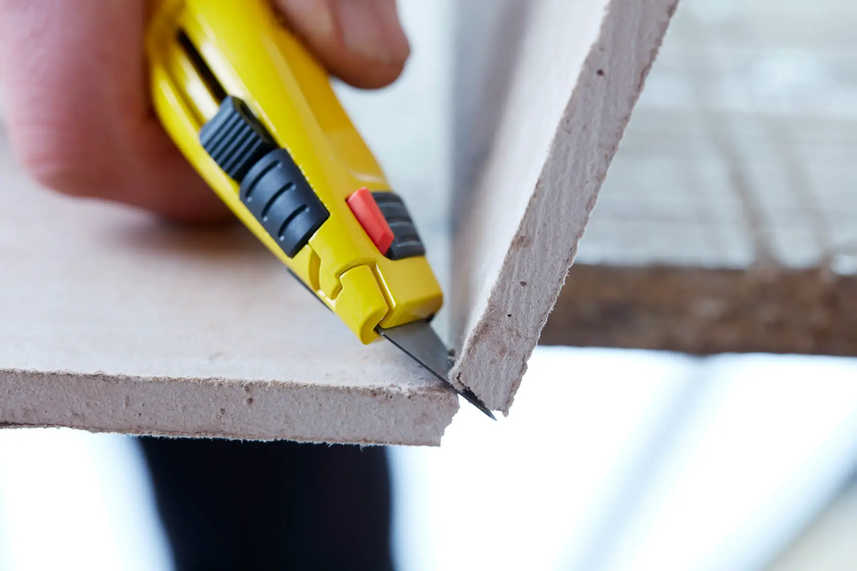 STANLEY 2-11-800 utility knife cutting drywall, close-up side angle.