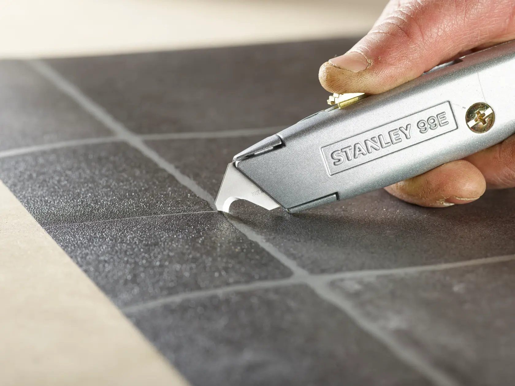 Photo of STANLEY 2-11-983 utility knife scoring black tile, close-up of blade and hand.