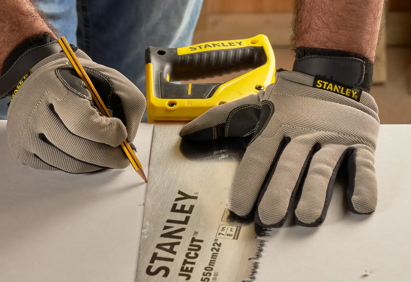 Stanley 2-20-037 JetCut Handsäge auf Tisch, Nahaufnahme, Arbeiter mit Handschuhen markiert Schnittlinie.