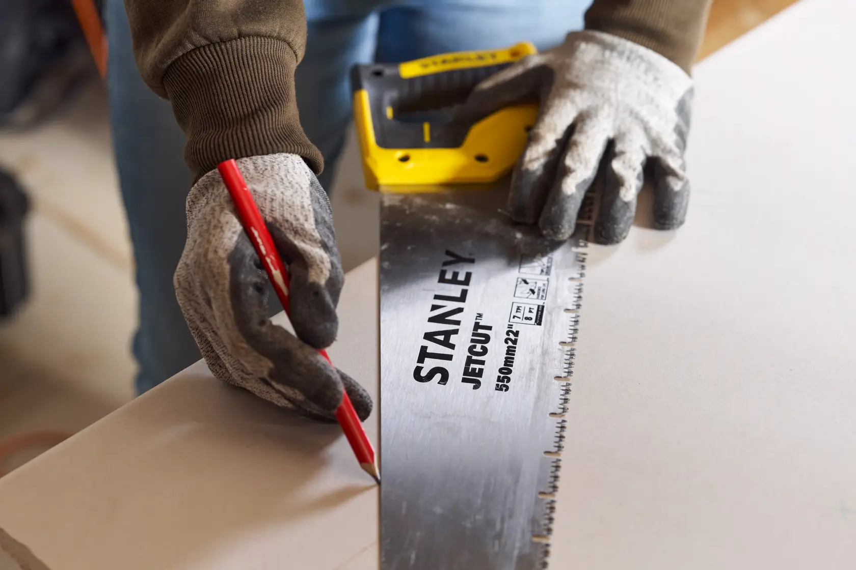 STANLEY 2-20-037 Handsäge mit gelb-schwarzem Griff, Nutzer mit Handschuhen markiert Holz mit rotem Bleistift.